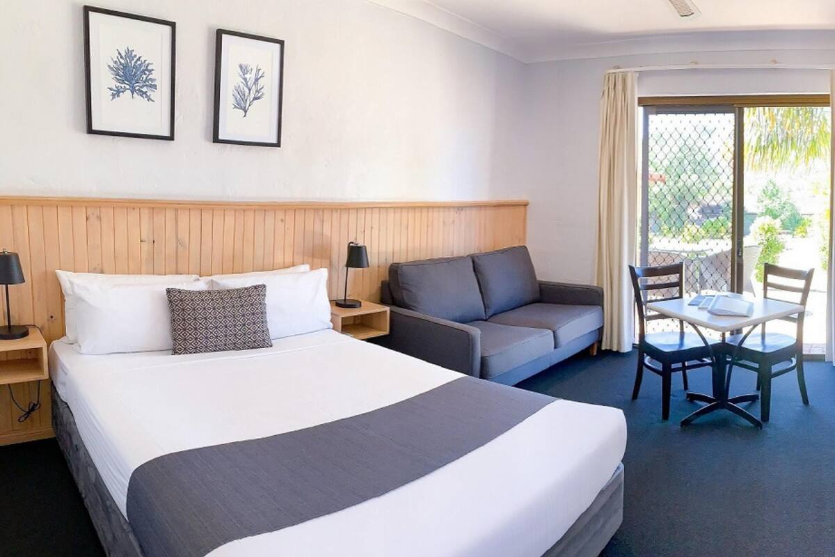 A hotel room with a large bed, a sofa, a dining table, and two framed botanical prints on the wall.