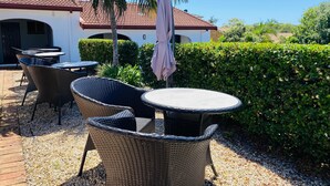 An outdoor patio with wicker furniture and a table, surrounded by gravel and greenery. - Costa Rica Motel (South West Rocks)