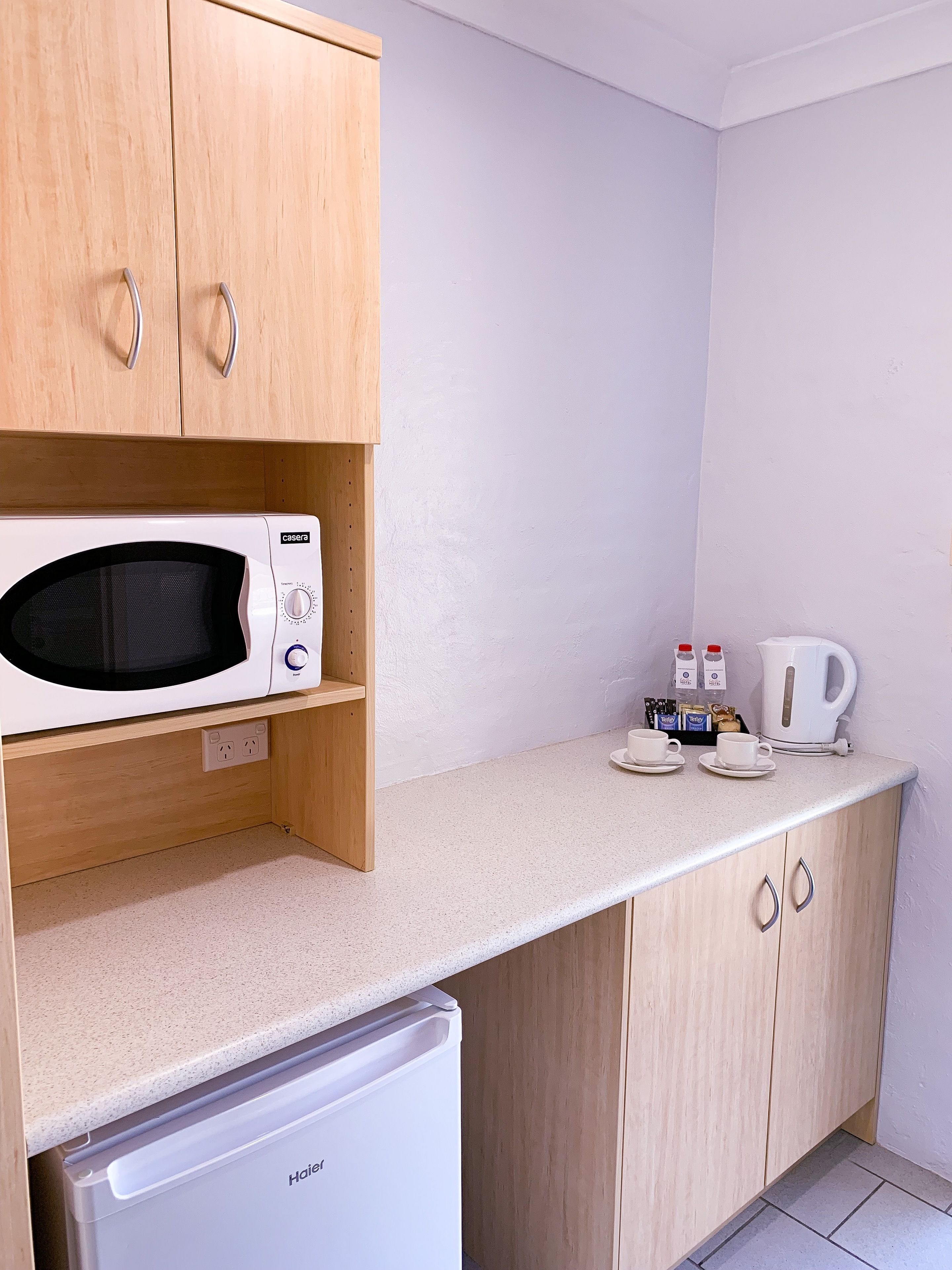 A compact kitchen with wooden cabinets, a microwave, a coffee maker, and a small refrigerator.