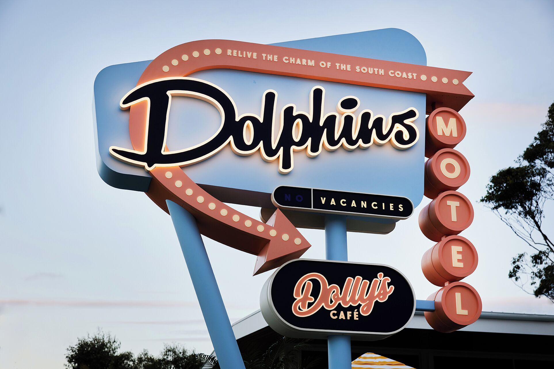 Placa de motel com os textos 'Dolphins' e 'Dolly's Café', um aviso de 'Sem Quartos Disponíveis' e um design retro clássico.