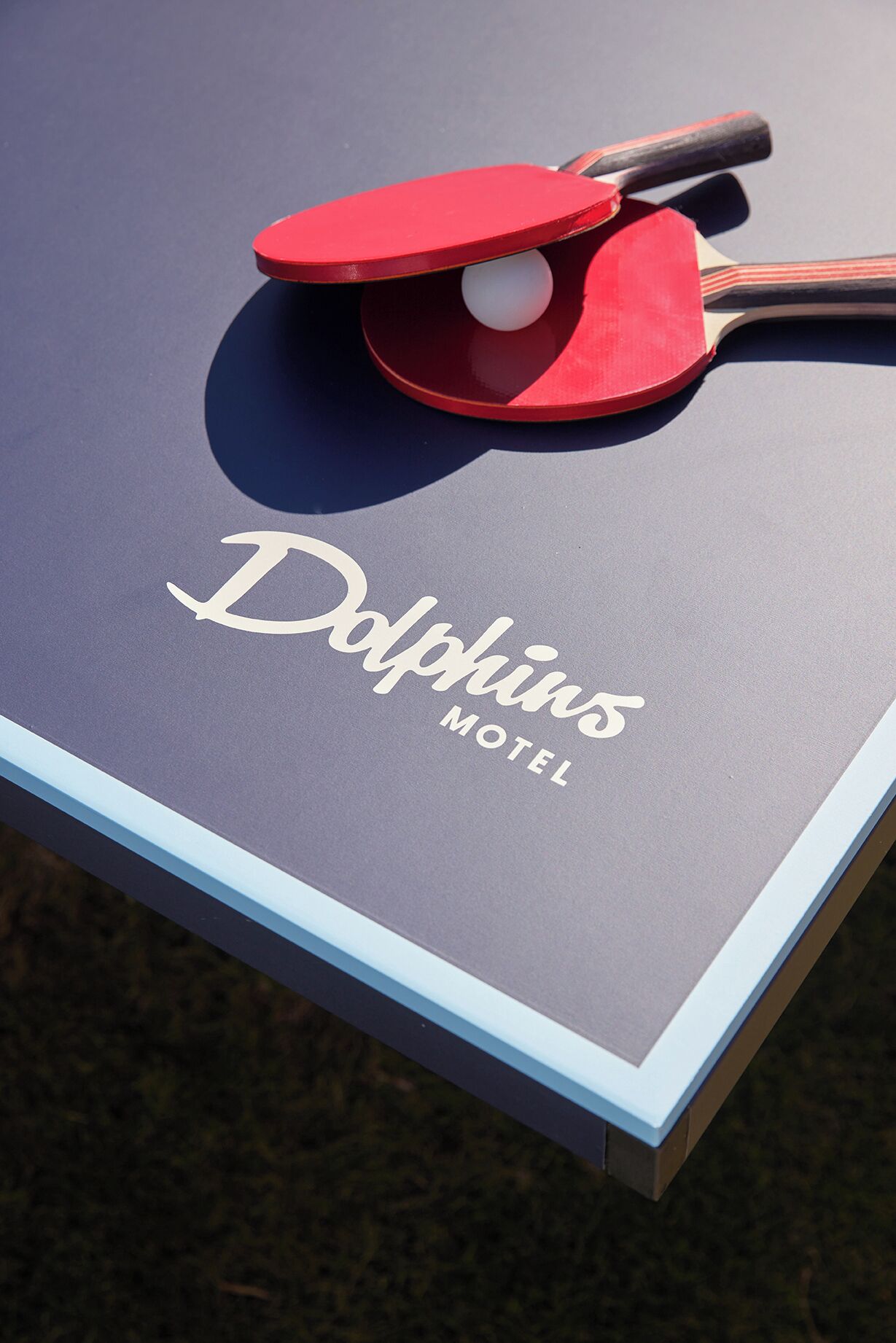 Una mesa con una pala y una pelota, y el texto 'Dolphins Motel' sobre una superficie oscura.