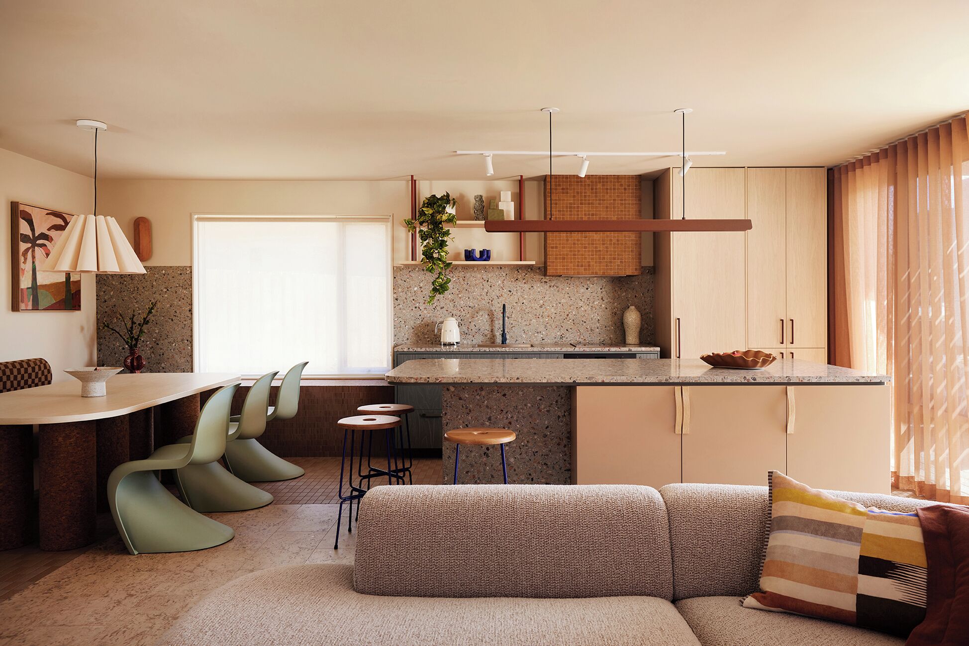 Una cocina moderna con una isla central, taburetes de bar, un sofá y una mesa de comedor.