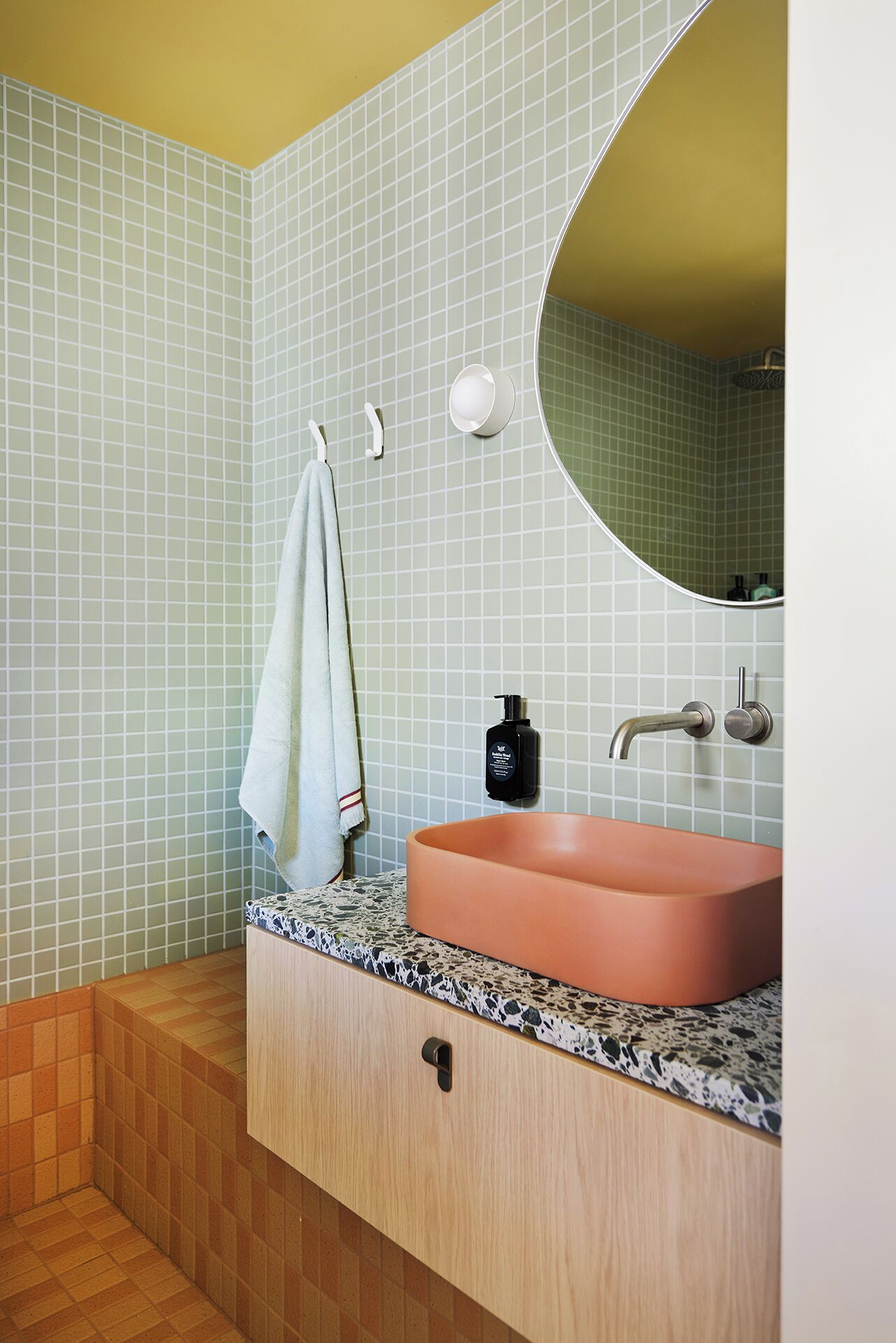 Une salle de bain avec un miroir rond, un lavabo et une serviette accrochée à un crochet.
