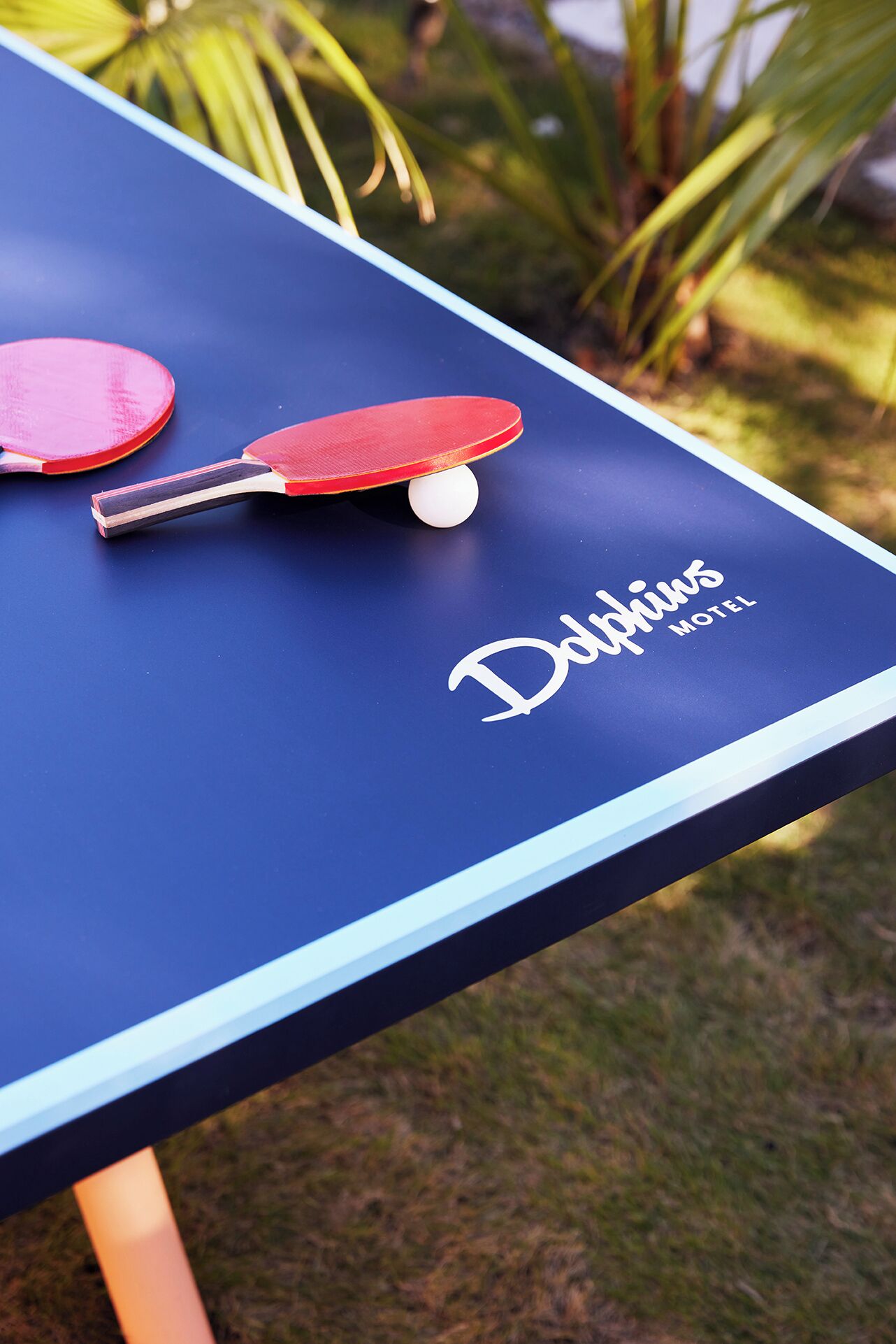 A blue ping pong table with a white ball and two red paddles.