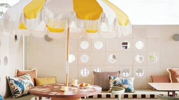 An outdoor patio with a wooden ceiling, a round table, two chairs, and a yellow and white umbrella.