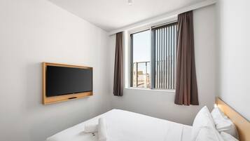 Een hotelkamer met een bed, een aan de muur bevestigde televisie en een raam met gordijnen.