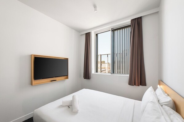 A hotel room with a bed, a TV mounted on the wall, and a window with curtains. - YHA Sydney Harbour (The Rocks)
