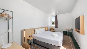 Una habitación de hotel moderna con una cama grande, un escritorio, una silla, un televisor y una ventana con cortinas.
