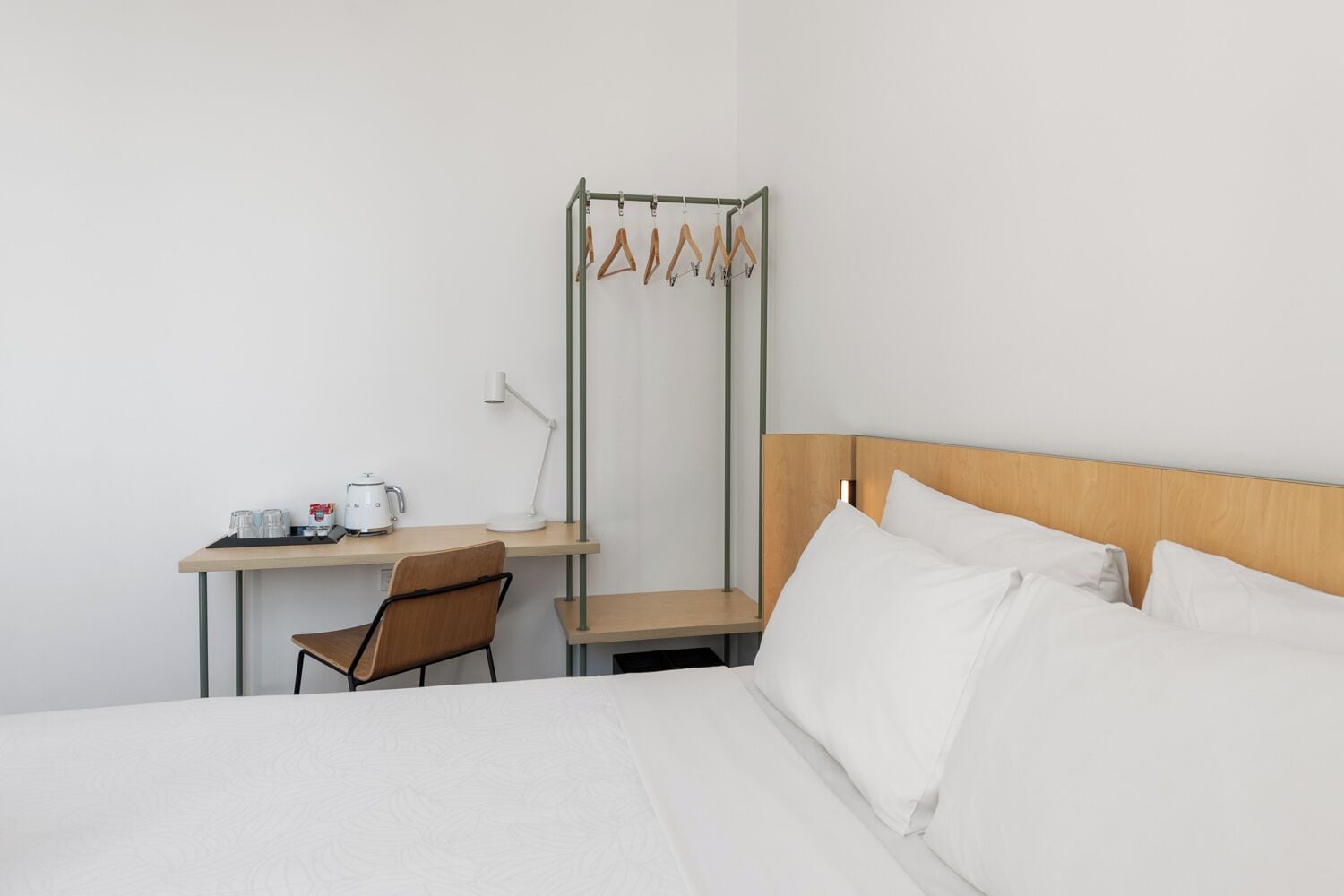 A hotel room with a bed, a desk with a chair, a coffee maker, and a hanging clothes rack.