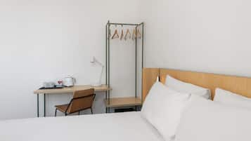 A hotel room with a bed, a desk with a chair, a coffee maker, and a hanging clothes rack.