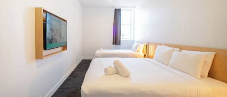 A hotel room with two beds, a flat-screen TV mounted on the wall, a window with curtains, and a carpeted floor.