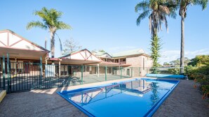 A swimming pool with a fenced area, surrounded by buildings with red roofs and palm trees. - Allan Cunningham Motel (Kearneys Spring)