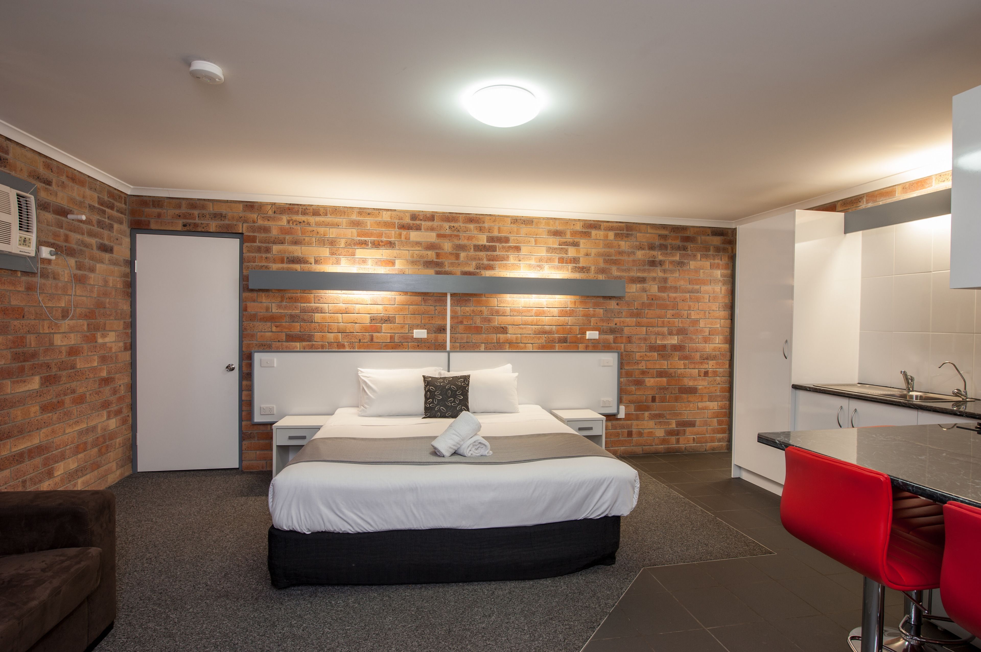 Ein Hotelzimmer mit Backsteinwand, einem Bett mit weißer Bettwäsche, einem roten Barhocker und einem weißen Waschbecken.