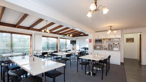 A spacious dining area with multiple tables and chairs, a kitchen area with modern appliances, and large windows providing natural light. - Allan Cunningham Motel (Kearneys Spring)
