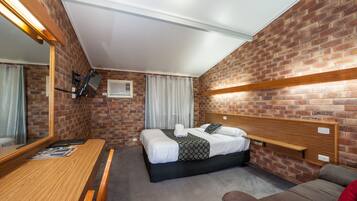 A hotel room with a brick wall, a wooden headboard, a bed with white linens, a wooden desk, and a brown sofa.