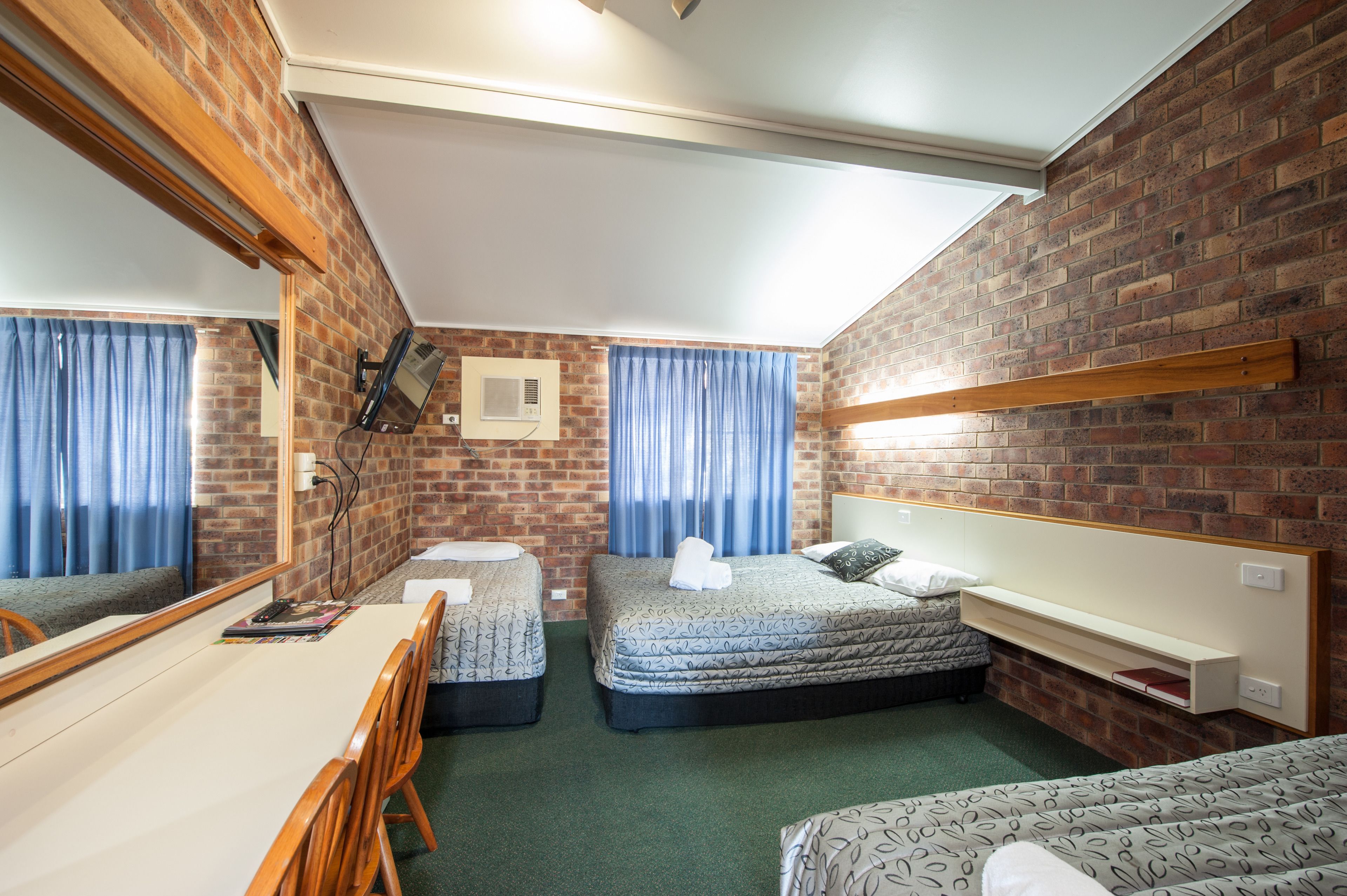 Habitación de hotel pequeña con pared de ladrillo, dos camas individuales, un escritorio y un espejo.