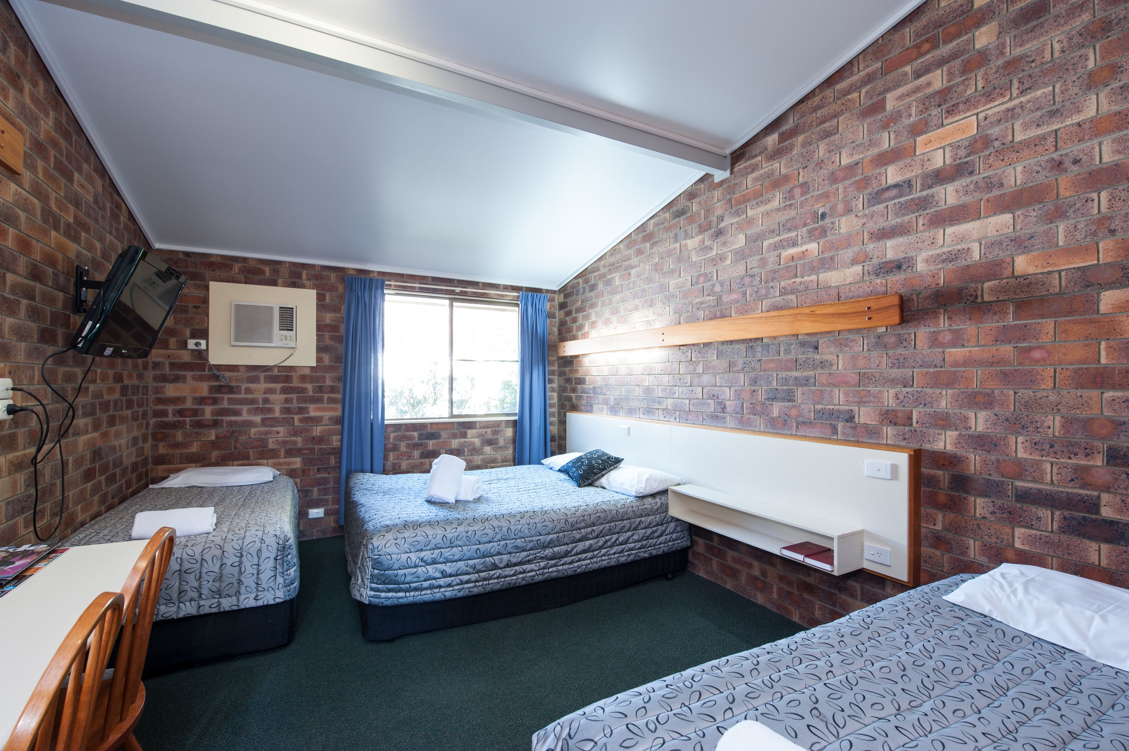 A room with two beds, a desk, and a brick wall.