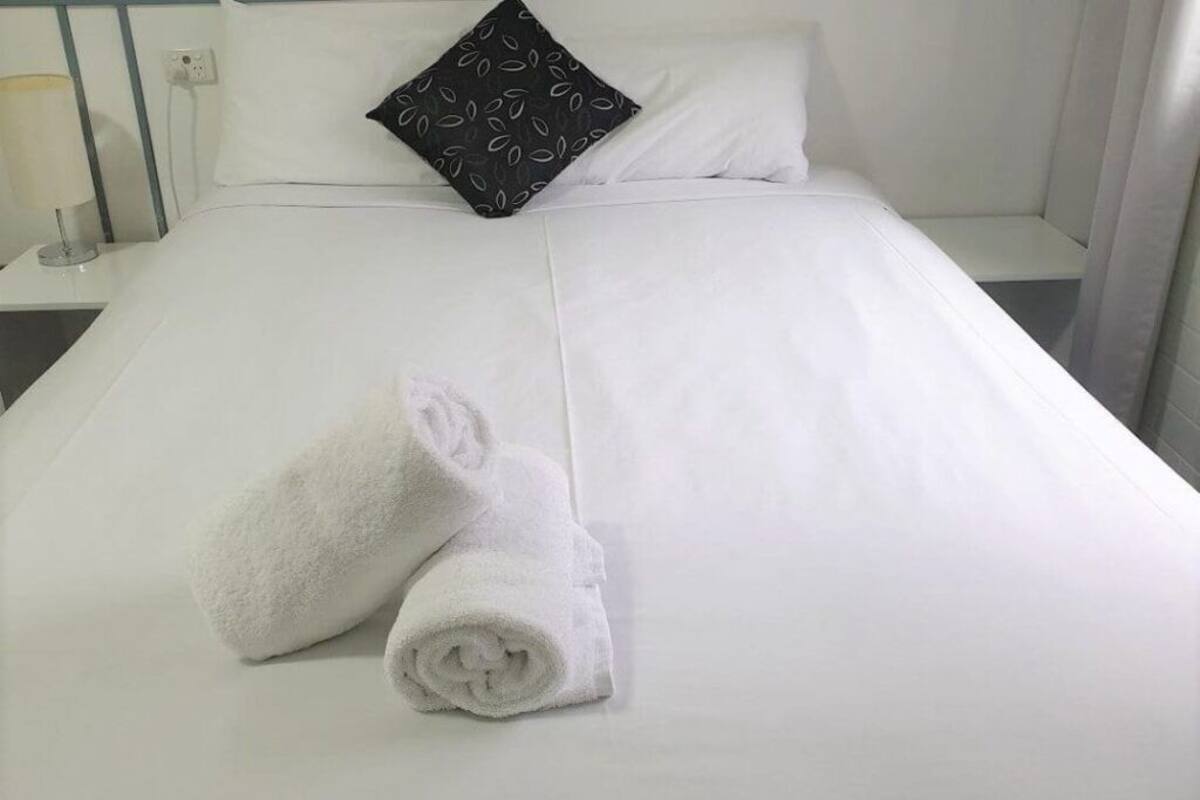 A neatly made bed with white linens and two rolled towels placed on it.