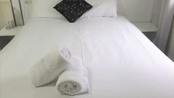 A neatly made bed with white linens and two rolled towels placed on it.