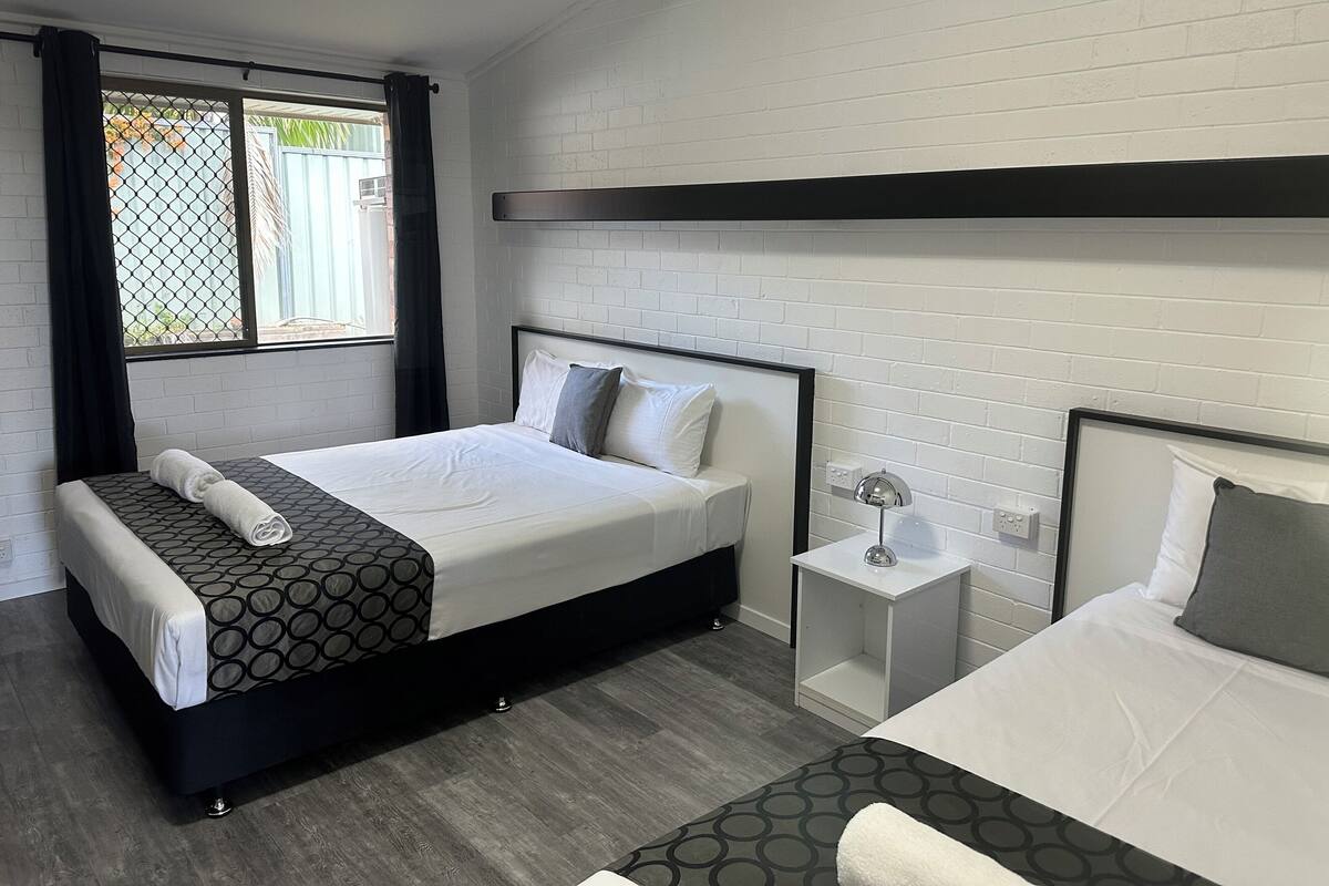 A modern hotel room with a large bed, a smaller bed, a nightstand, and a window with curtains.