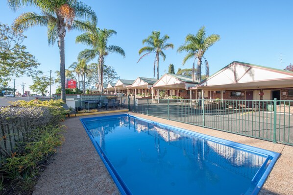 Una piscina con zona vallada, palmeras y un edificio de techo verde.