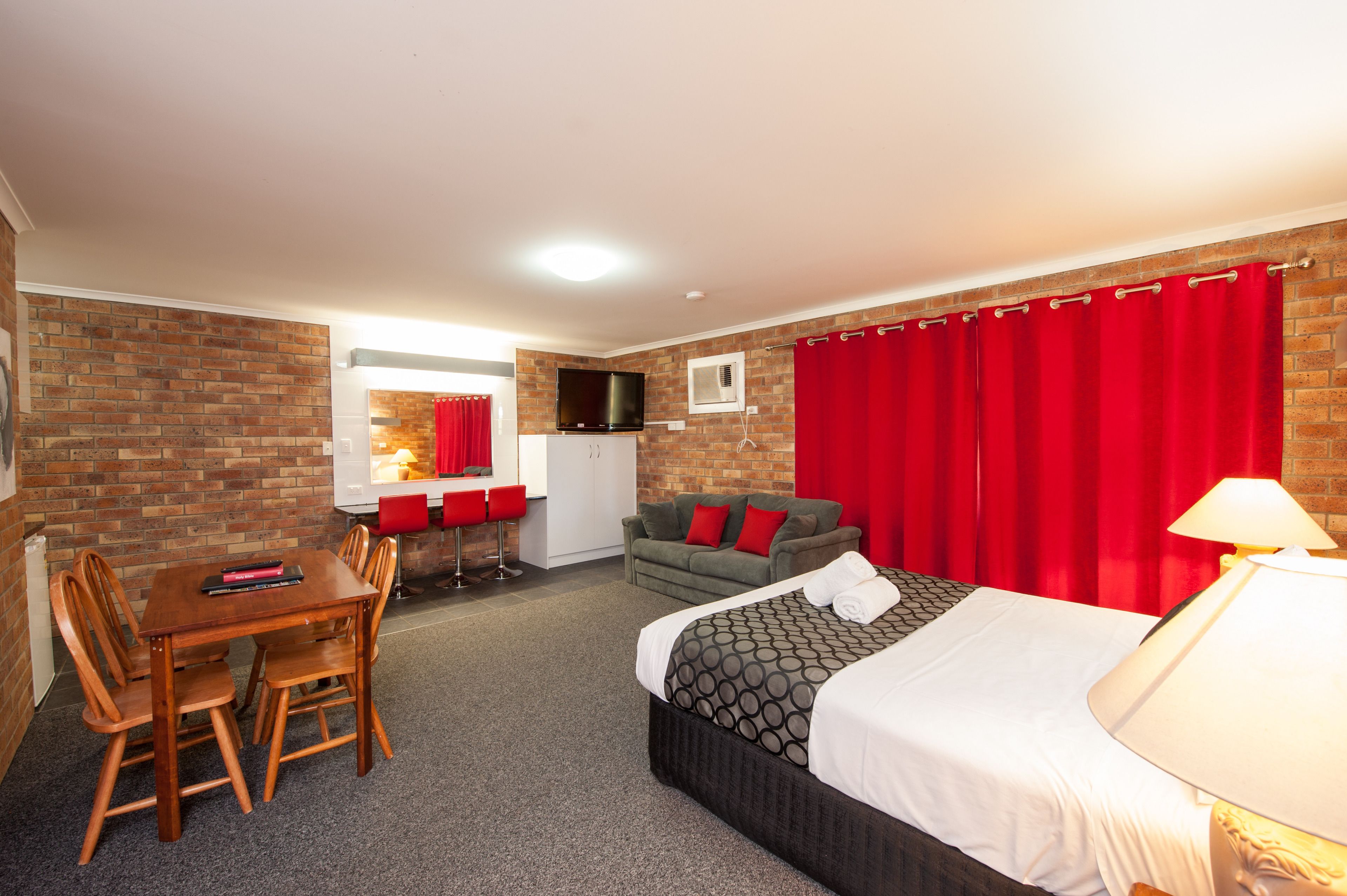 A hotel room with a bed, a dining table with chairs, a sofa, and a TV.