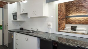 A modern kitchen with white cabinets, a black countertop, and a brick wall. - Allan Cunningham Motel (Kearneys Spring)