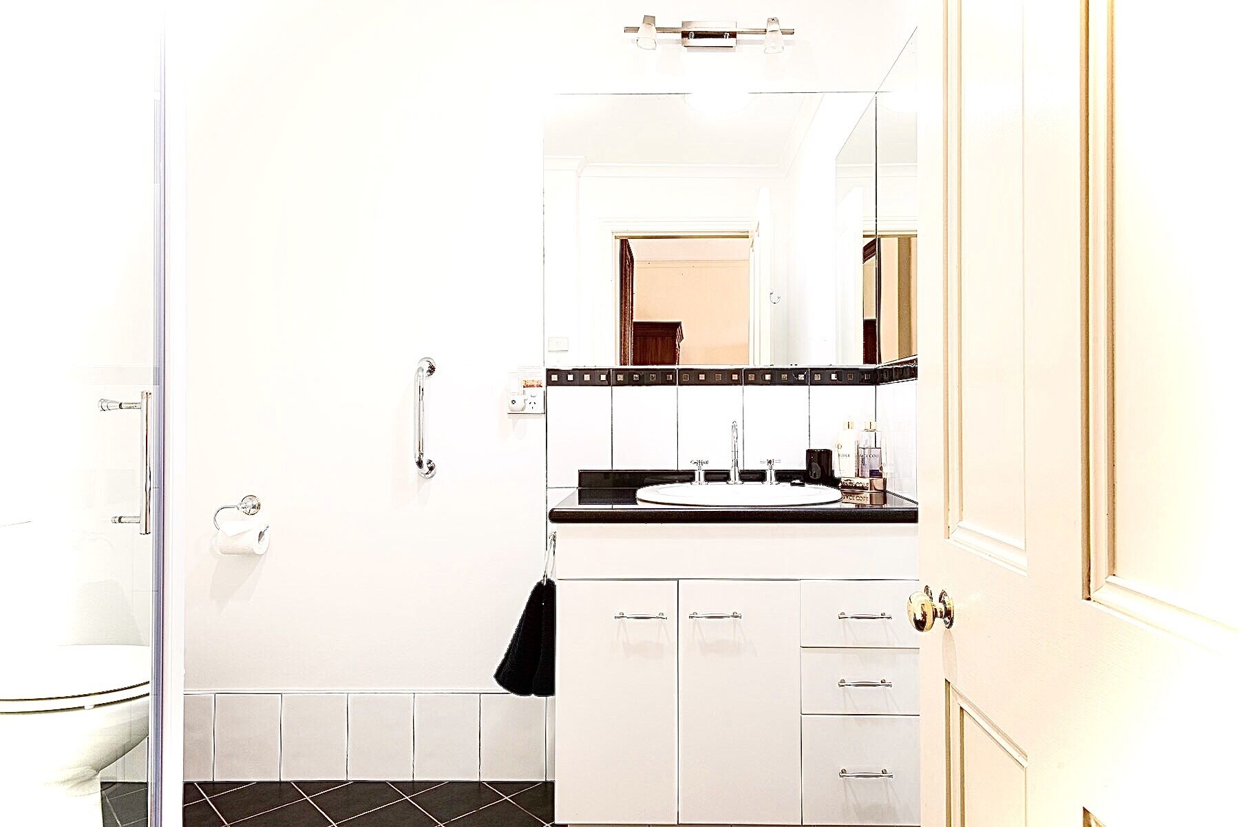 Een badkamer met een douchecabine van glas, een witte wastafel met een zwart aanrechtblad, en een spiegel boven de wastafel.