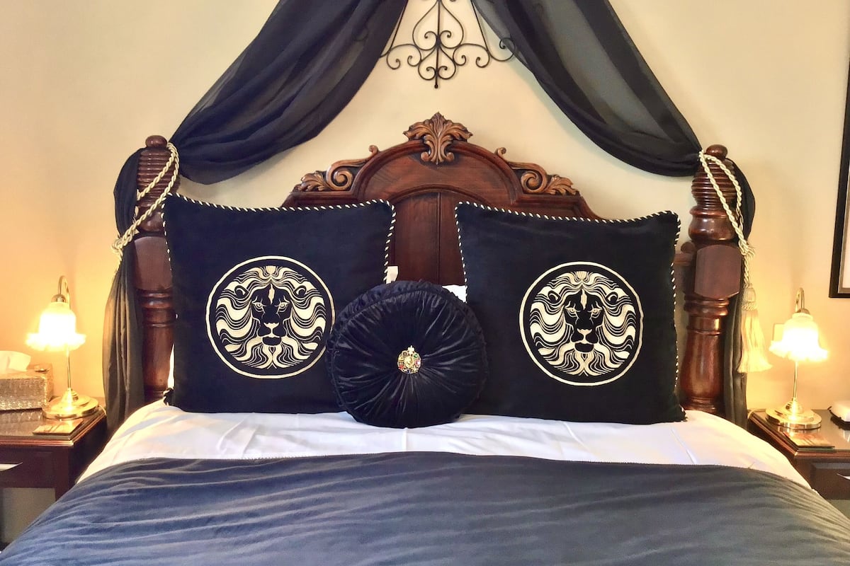A bed with a dark headboard, two decorative pillows with a lion design, and a black throw pillow.
