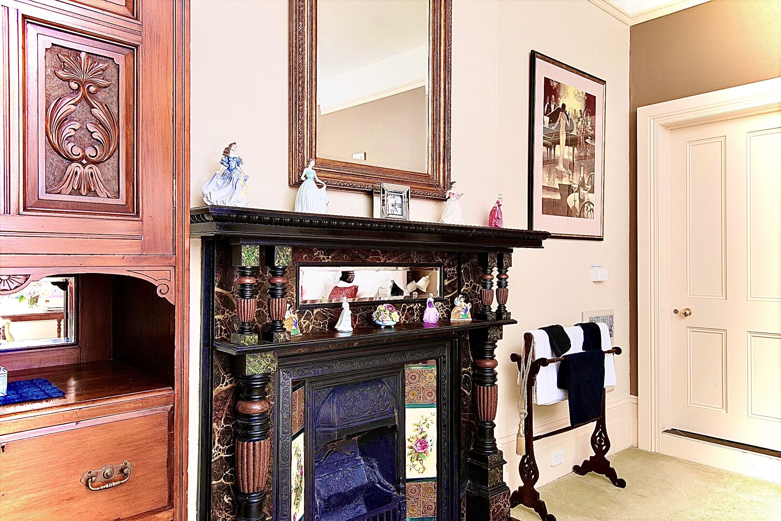 A room with a wooden dresser, a fireplace with a mirror above it, and a door with a towel rack.