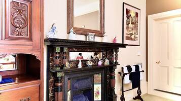 A room with a wooden dresser, a fireplace with a mirror above it, and a door with a towel rack.
