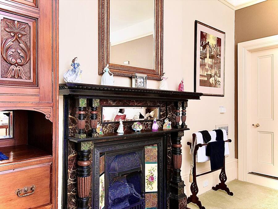 A room with a wooden dresser, a fireplace with a mirror above it, and a door with a towel rack.