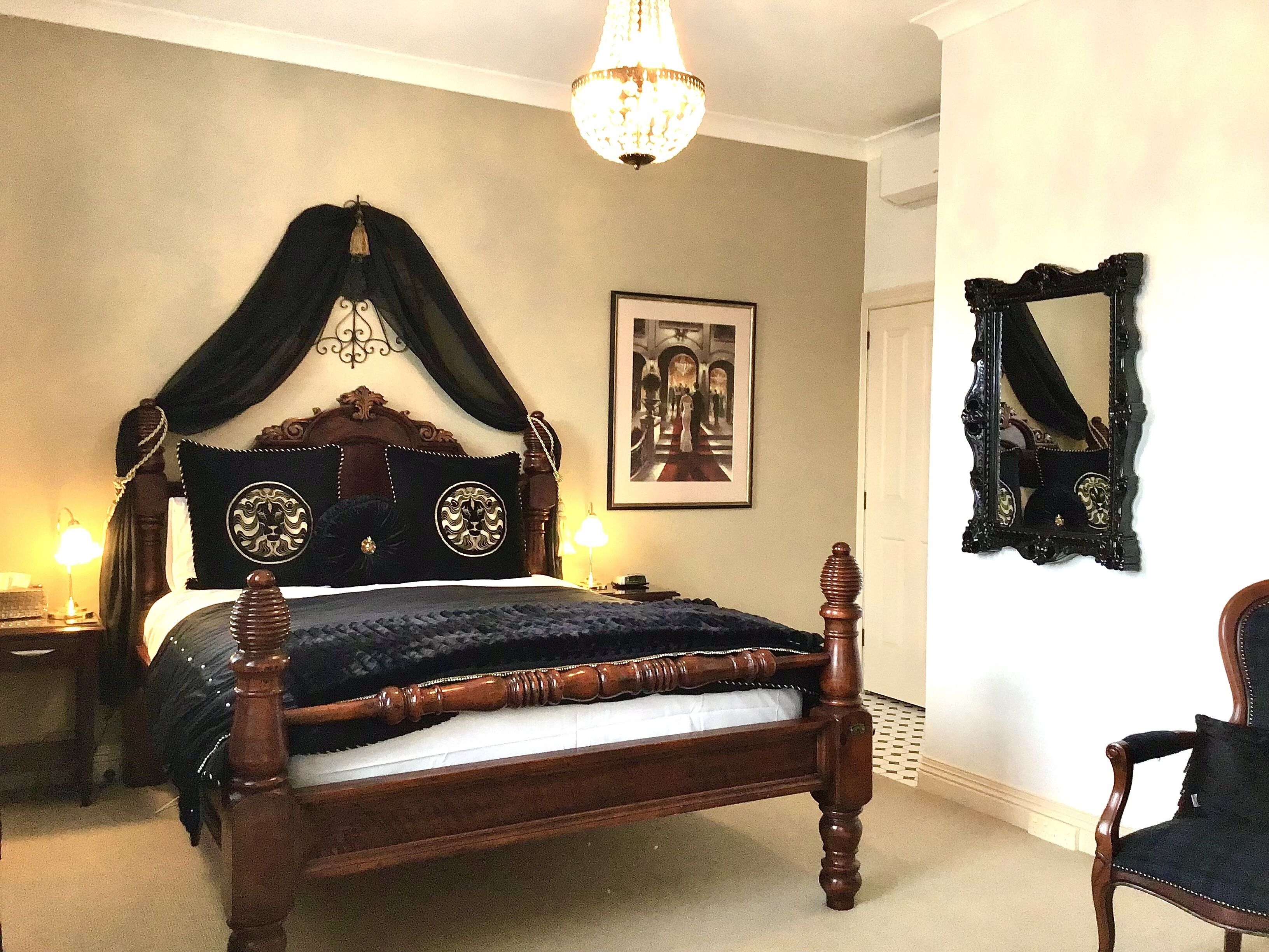 Un dormitorio con cama con dosel, candelabro, un cuadro en la pared y un espejo con marco ornamentado.