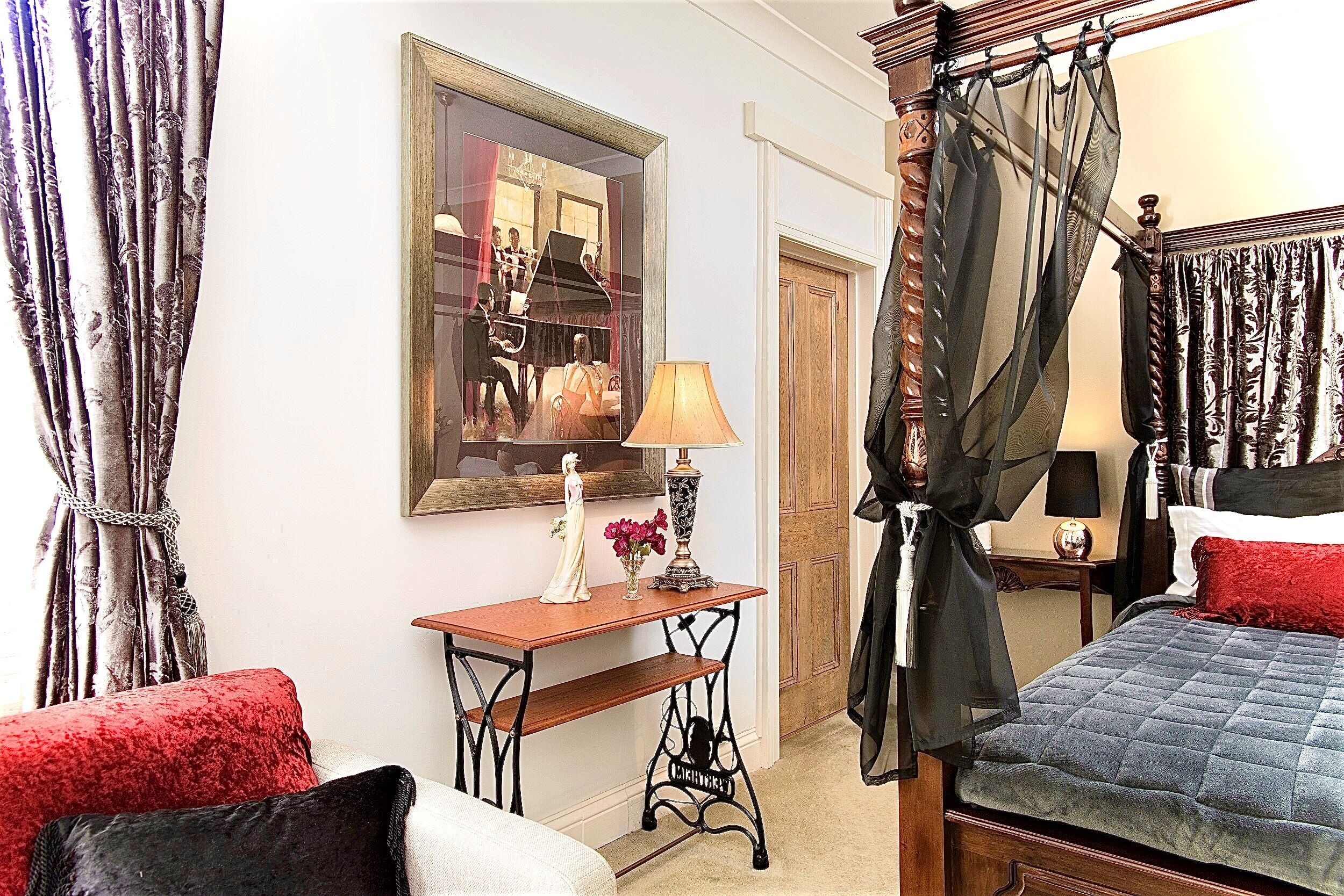 A bedroom with a bed, a nightstand, a lamp, a mirror, and curtains.