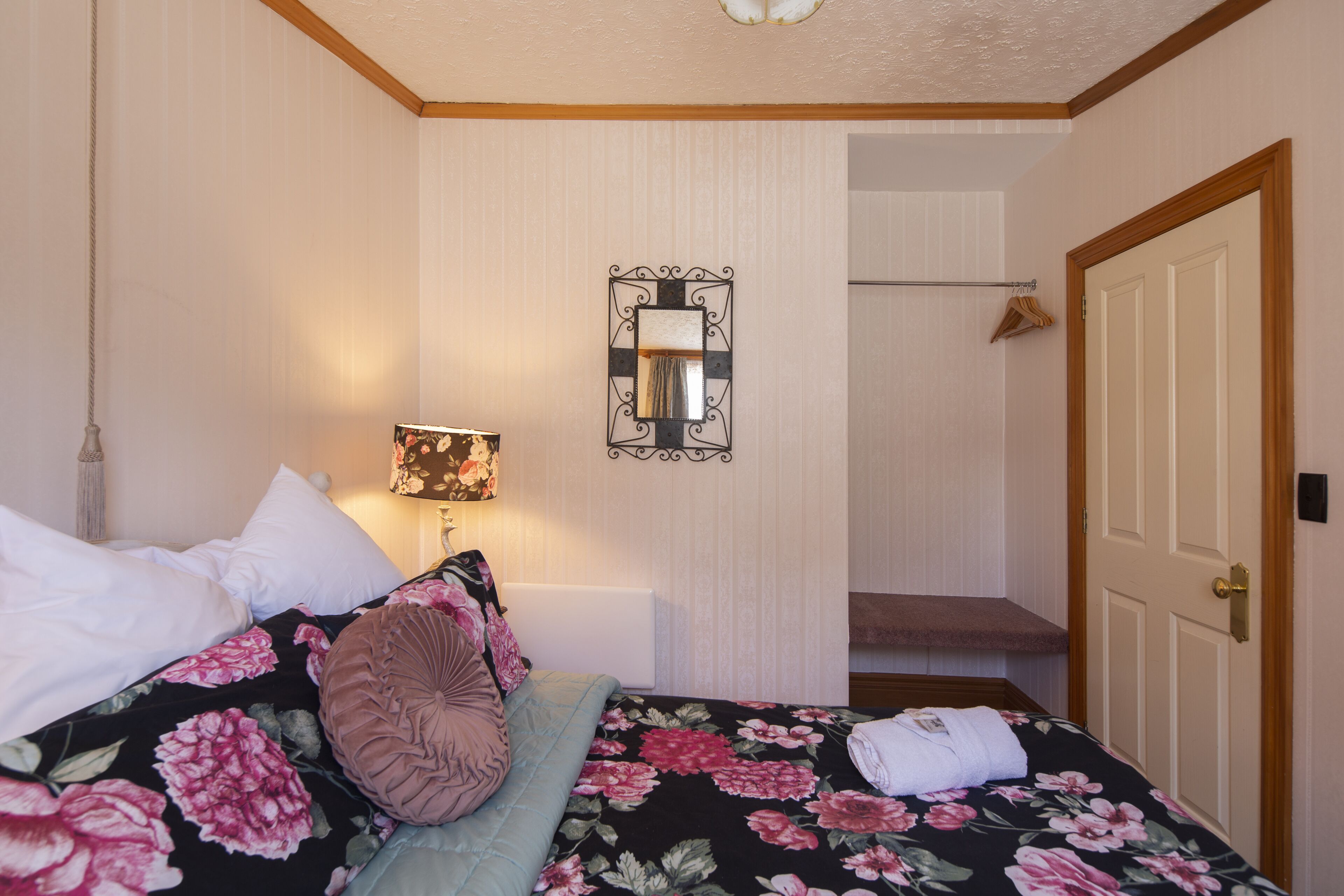 A hotel room with a bed, a hanging lamp, a mirror, and a door.