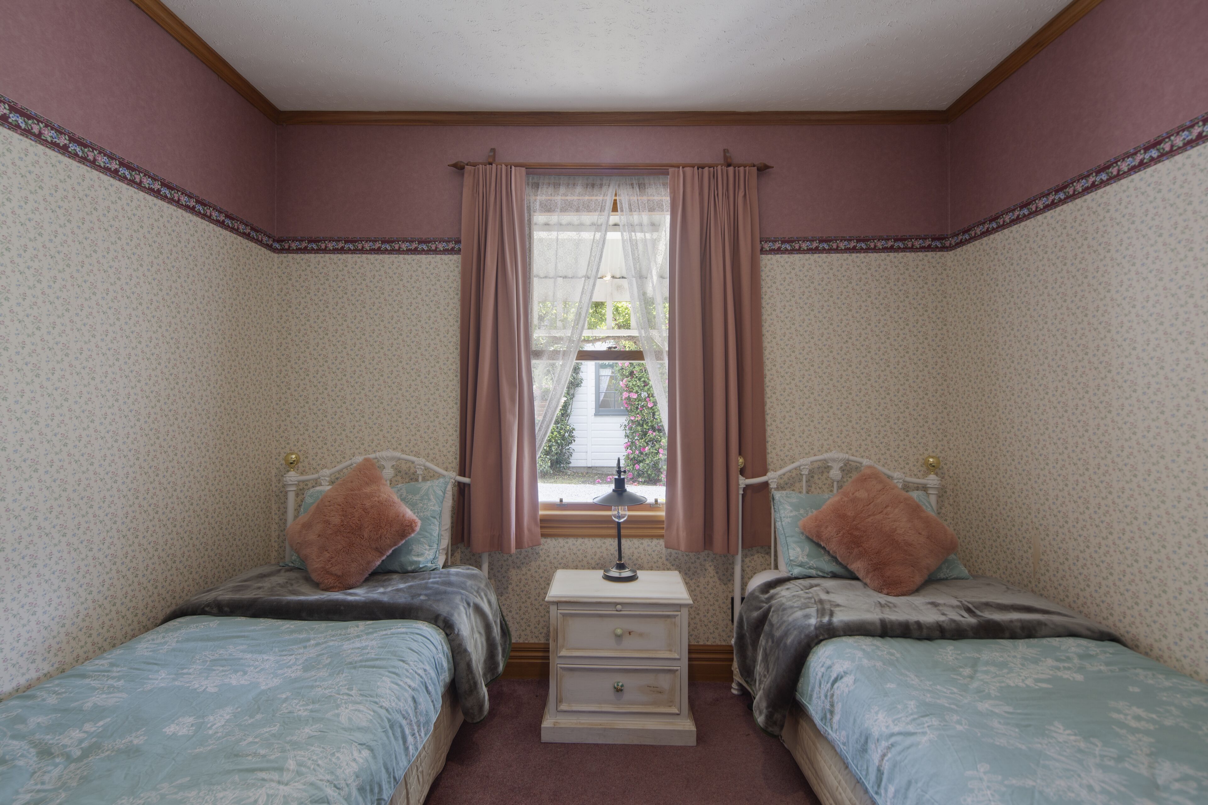 A bedroom with two beds, a nightstand, and a window with curtains.