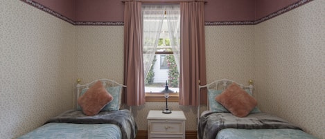 Een slaapkamer met twee bedden, een nachtkastje en een raam met gordijnen.