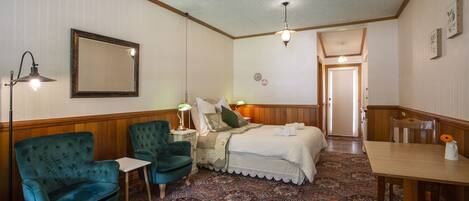 A bedroom with a bed, two chairs, a small table, a lamp, and a mirror.