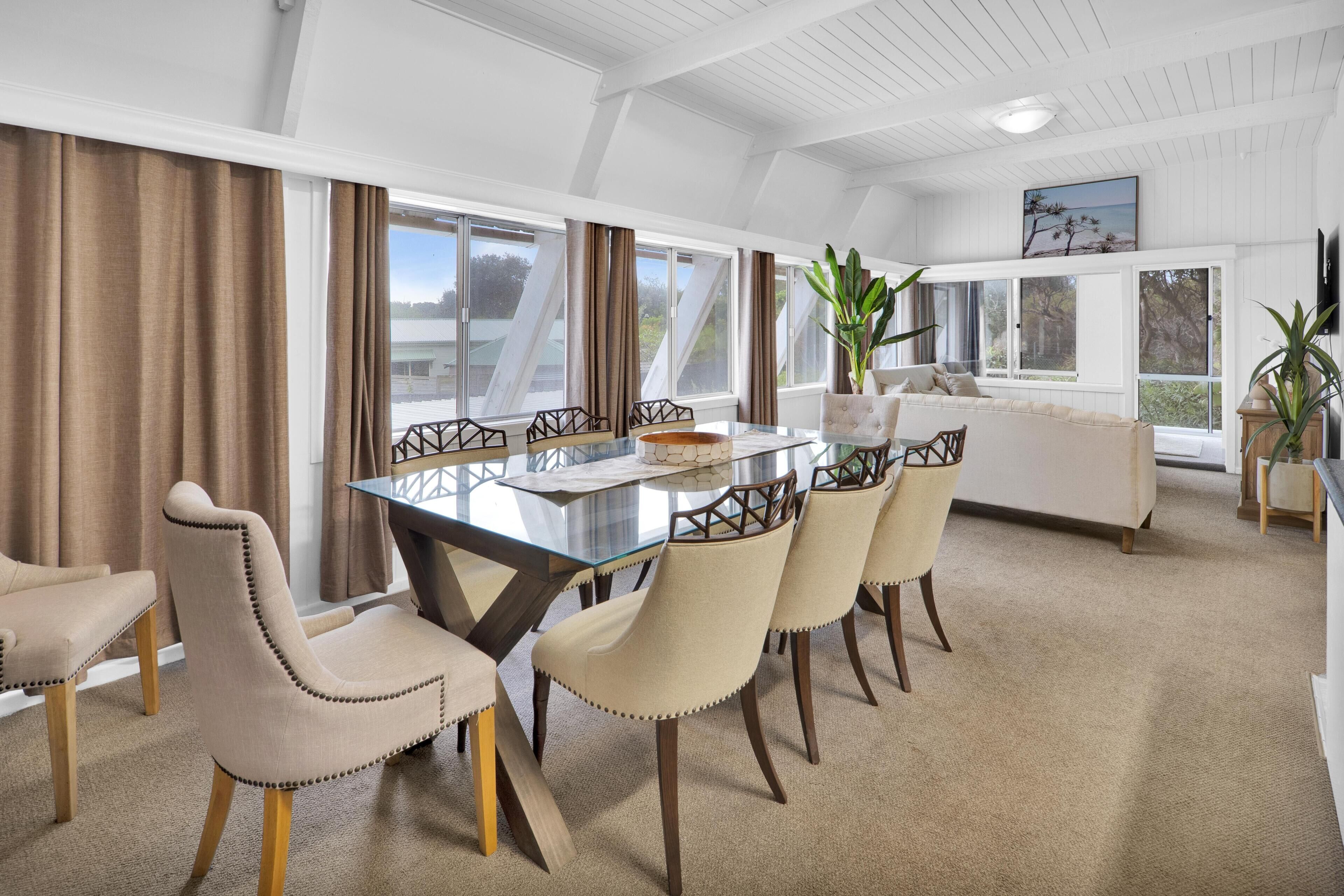 Un comedor con mesa de vidrio, sillas color beige y sofá blanco.