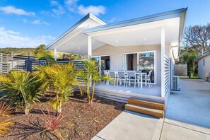 Una casa moderna con un porche cubierto, mobiliario de exterior y un jardín ajardinado.