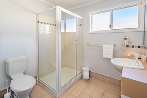 Un baño con ducha de vidrio, inodoro, lavamanos con espejo y ventana sobre el lavamanos.