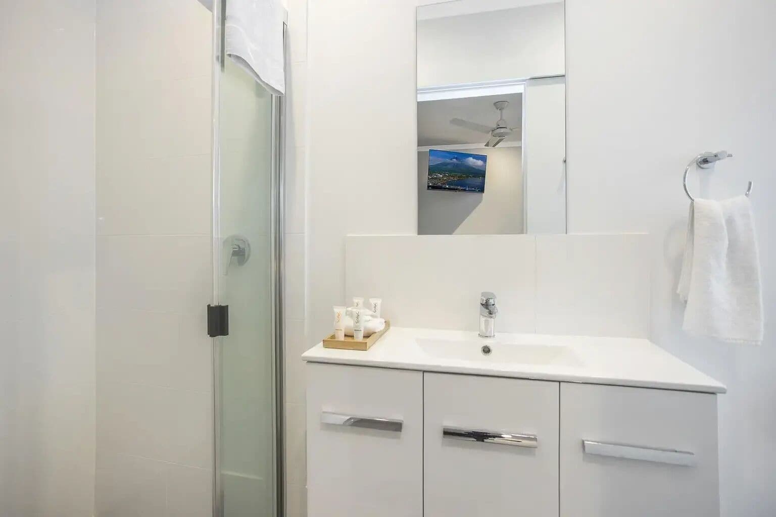 Un baño moderno con cabina de ducha de vidrio, un lavamanos blanco con espejo y un perchero para toallas.