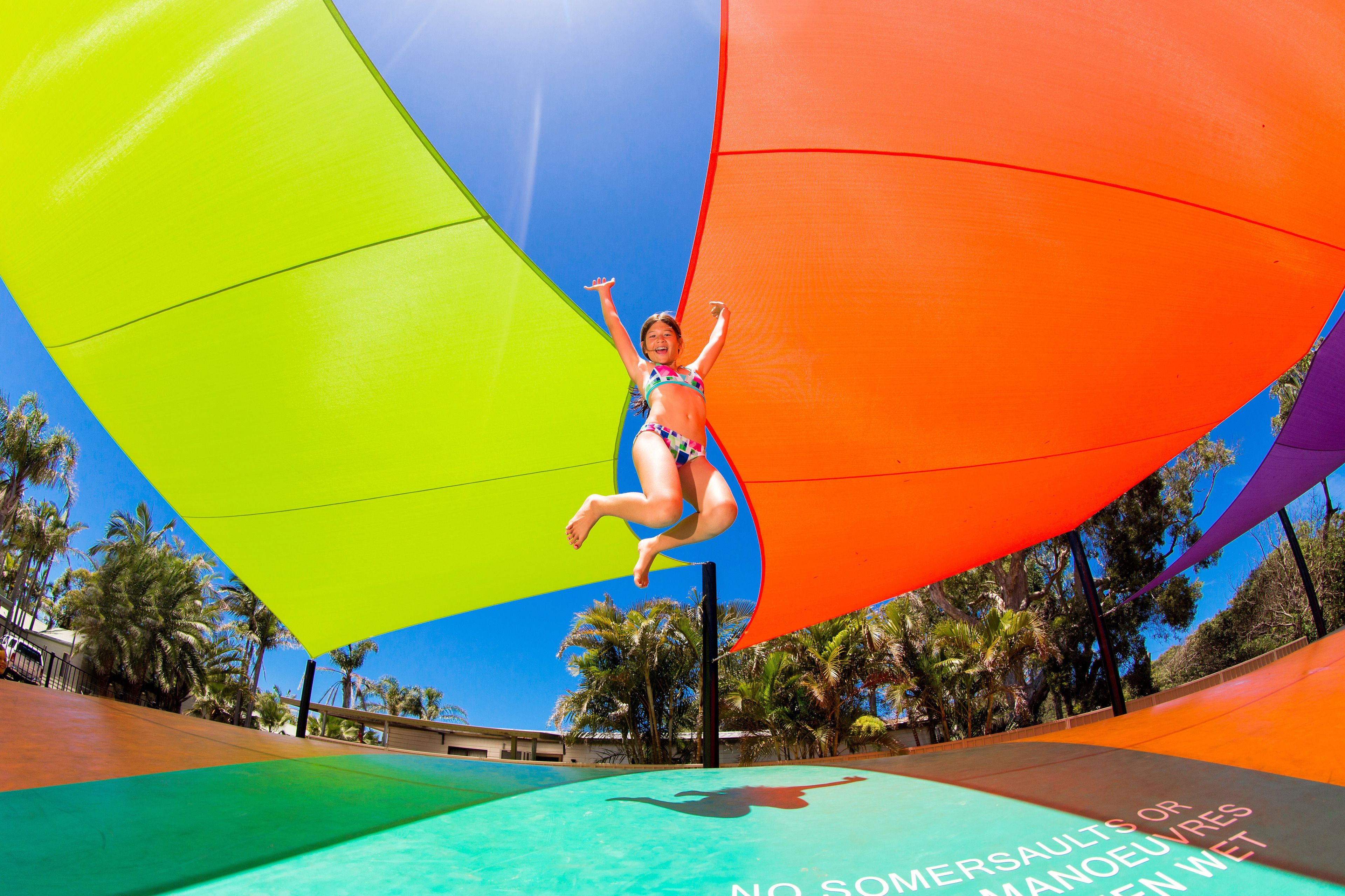 Una persona saltando desde un trampolín debajo de un toldo colorido.