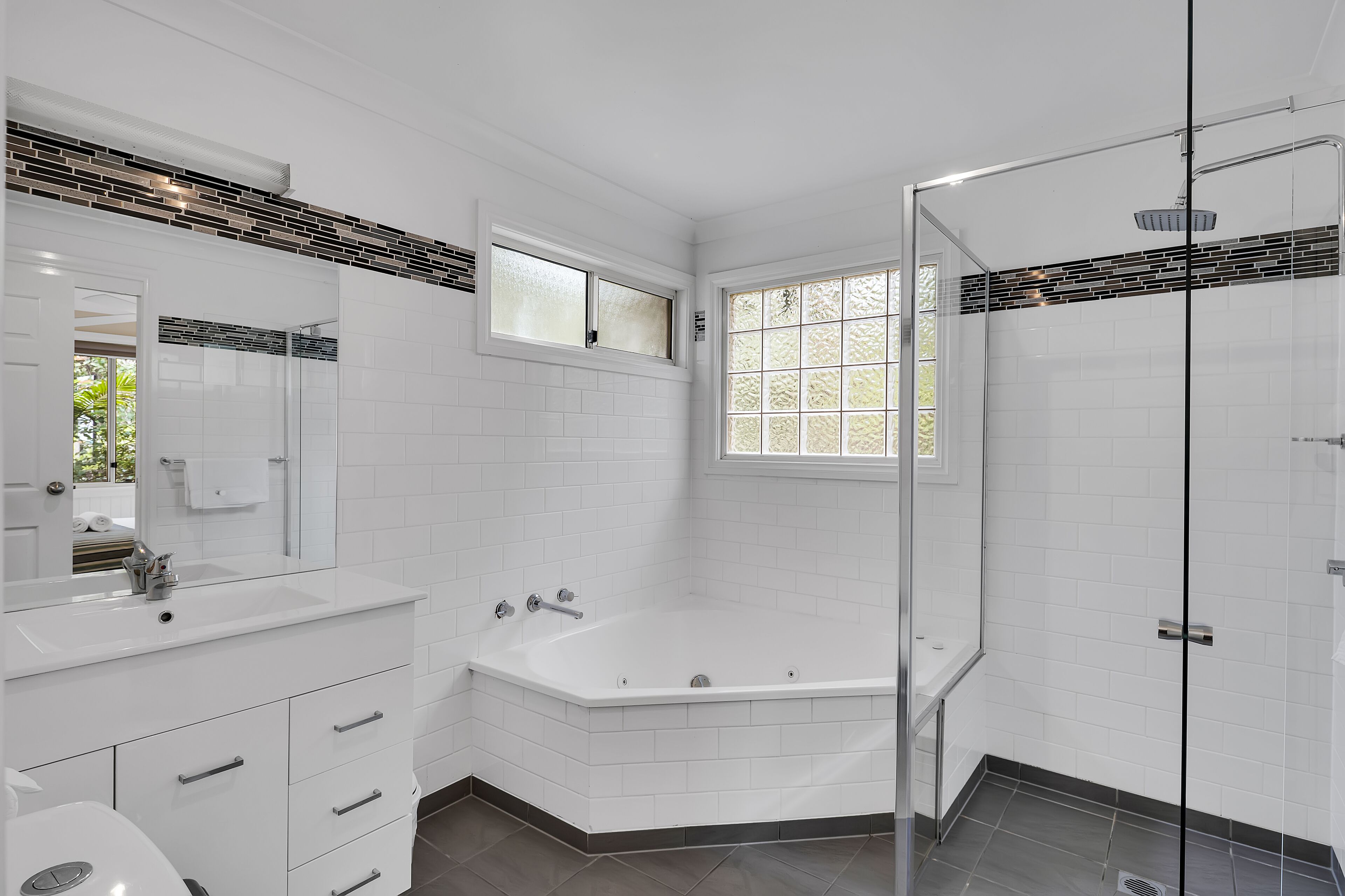 A modern bathroom with a white vanity, a large bathtub, a glass shower enclosure, and a window providing natural light.