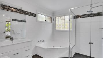 A modern bathroom with a white vanity, a large bathtub, a glass shower enclosure, and a window providing natural light.