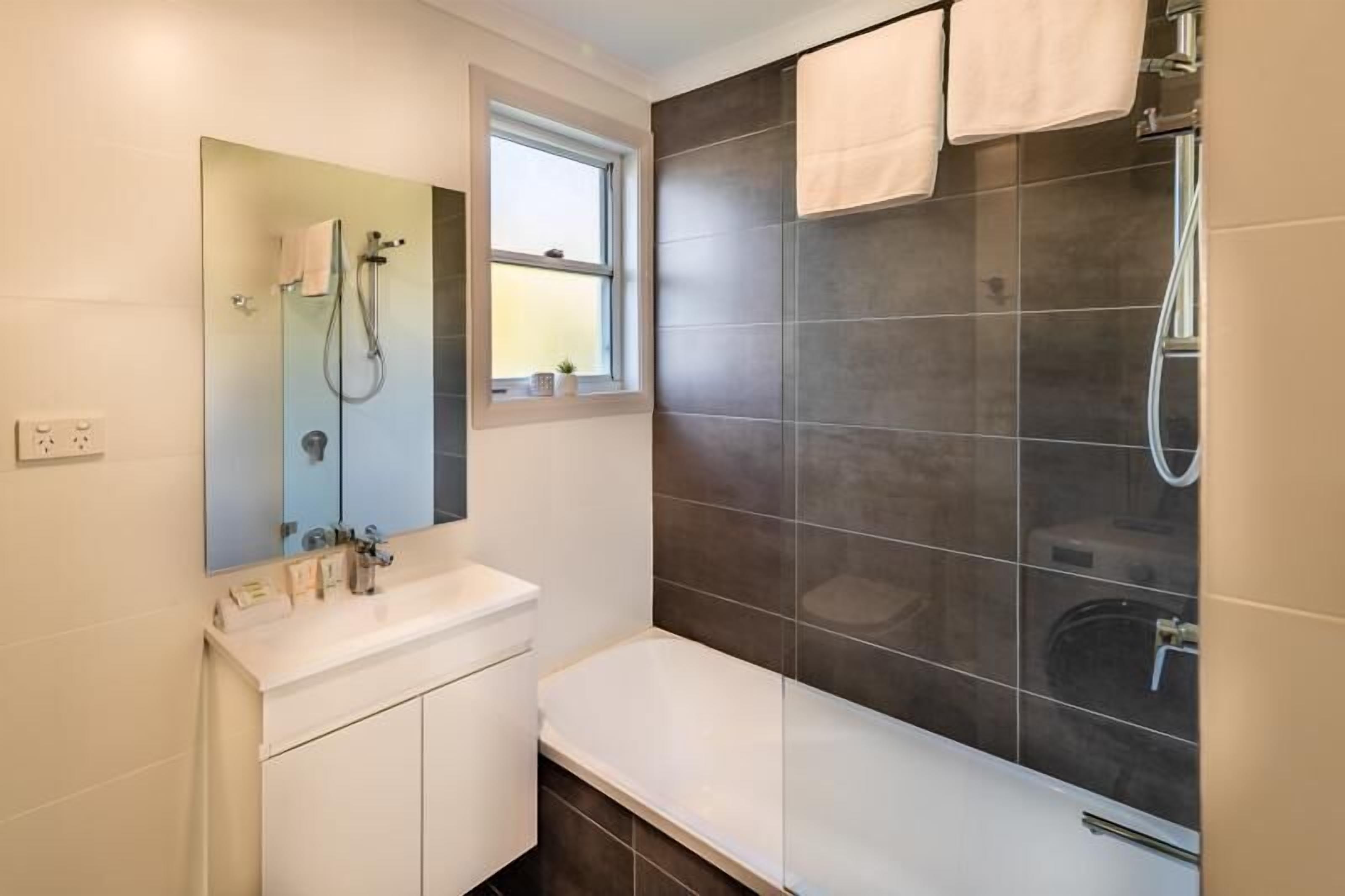 A modern bathroom with a white sink, mirror, and dark tiled shower area.
