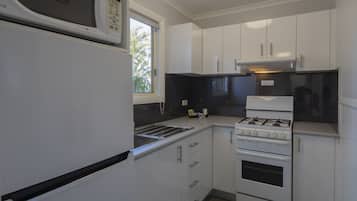 Cocina compacta con armarios blancos, microondas, cocina a gas y ventana que proporciona luz natural.