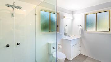 A modern bathroom with a glass shower enclosure, a toilet, a sink with a mirror, and a window.