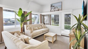 Un salón amplio con un sofá color beige, una mesa de centro y ventanas grandes que ofrecen vistas al exterior.