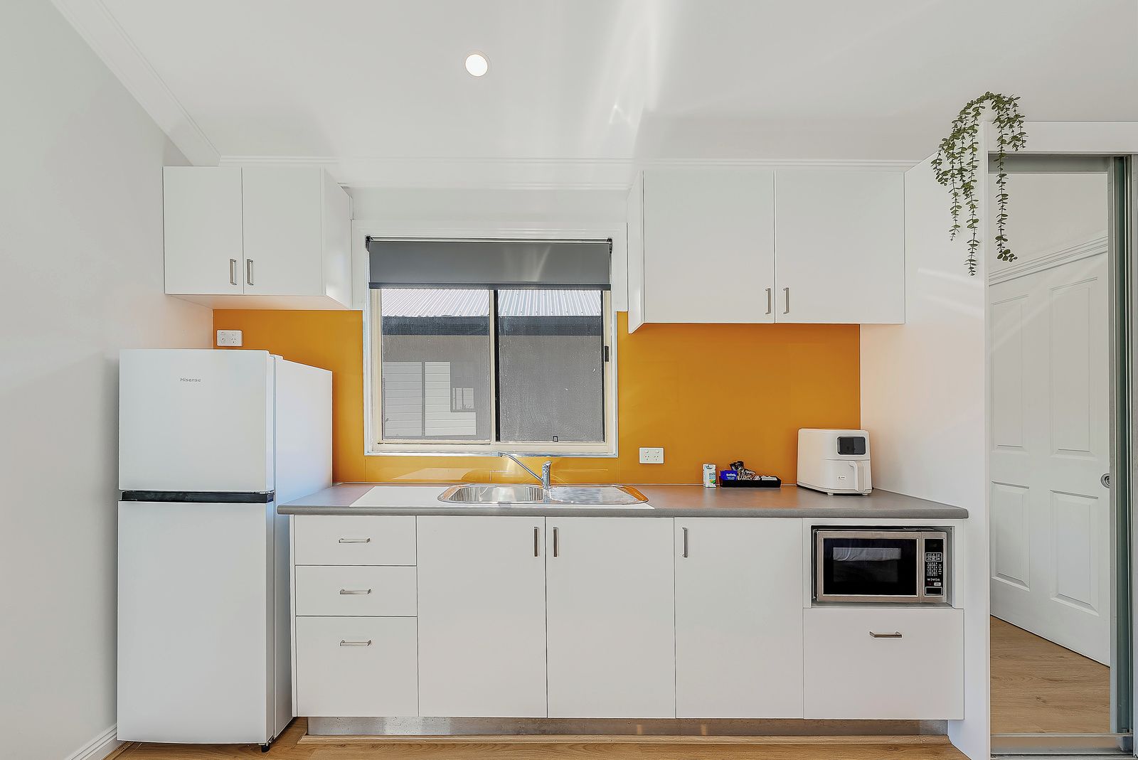 A compact kitchen with white cabinets, a built-in oven, a microwave, and a window with a view.